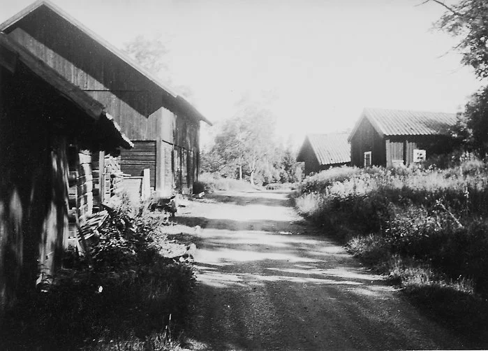 Svartvitt foto från 1967: en grusväg mellan gamla timrade lador och uthus vid Krusboda torp, innan radhusområdet byggdes.
